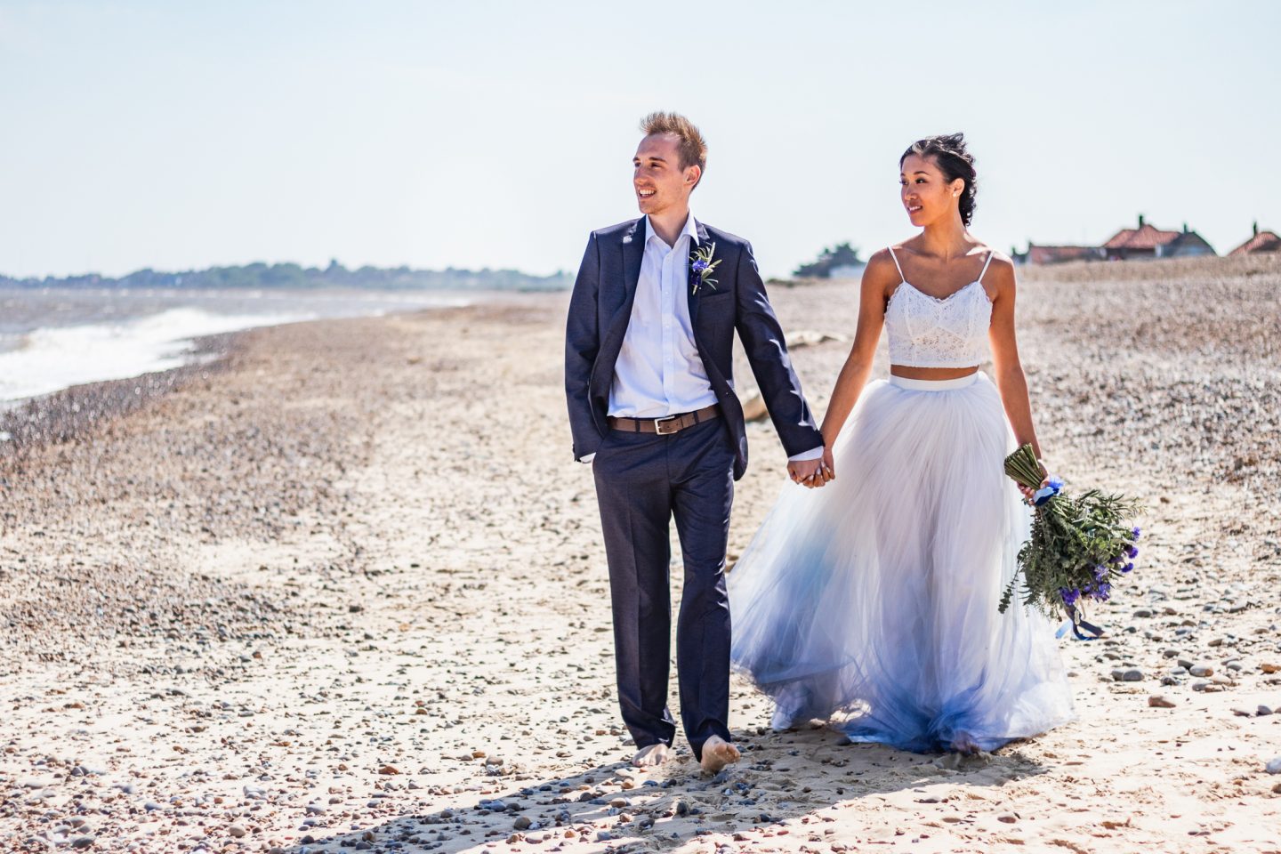 wedding couple walking on the beach wearing blue wedding dress.